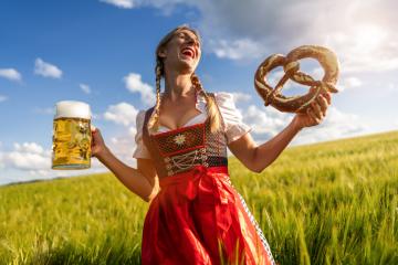 Laughing woman in traditional Bavarian tracht holding beer mug and big pretzel in a sunny wheat field ready for Oktoberfest festival in munich, germany- Stock Photo or Stock Video of rcfotostock | RC Photo Stock