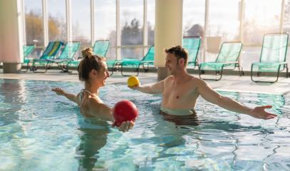 Male trainer conducting aquatic therapy with a female client using exercise balls in a sunny pool- Stock Photo or Stock Video of rcfotostock | RC Photo Stock