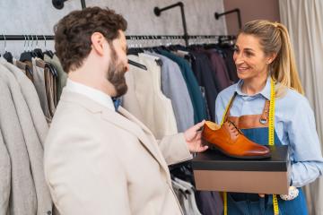 man examines a tan dress shoe presented by a tailor holding a measuring tape at a store : Stock Photo or Stock Video Download rcfotostock photos, images and assets rcfotostock | RC Photo Stock.: