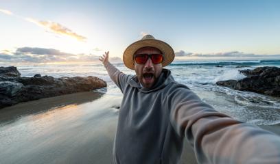 Man in a straw hat and sunglasses taking a selfie on a rocky beach at sunset enjoying summer holidays - Stock Photo or Stock Video of rcfotostock | RC Photo Stock