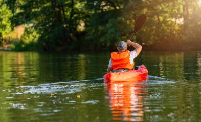 Man in an orange life jacket paddling a red kayak on a calm river, surrounded by lush greenery in sunlight. Kayak Water Sports concept image- Stock Photo or Stock Video of rcfotostock | RC Photo Stock