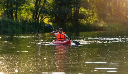 Man in orange life jacket paddles a red kayak through calm river waters, dappled with sunlight and surrounded by lush foliage in bavaria germany. Kayak Water Sports concept image- Stock Photo or Stock Video of rcfotostock | RC Photo Stock