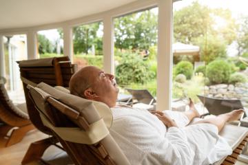man relaxing in a spa lounge hotel chair, eyes closed, dressed in a white robe with a serene garden in the background- Stock Photo or Stock Video of rcfotostock | RC Photo Stock