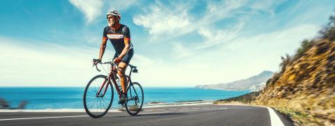 Mature Adult on a racing bike climbing the hill at mediterranean sea landscape coastal road- Stock Photo or Stock Video of rcfotostock | RC Photo Stock