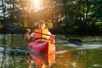 Mature man in orange life vest kayaking on a tranquil river, trees and sunlight in the background. Kayak Water Sports concept image- Stock Photo or Stock Video of rcfotostock | RC Photo Stock