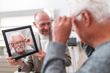 Optician holding a mirror for a older customer trying on glasses in a optician store- Stock Photo or Stock Video of rcfotostock | RC Photo Stock
