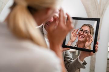 Optician holding a mirror to smiling woman trying on glasses in a optical store.- Stock Photo or Stock Video of rcfotostock | RC Photo Stock