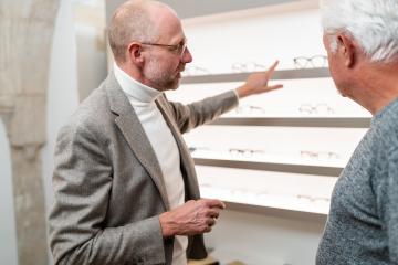 Optician pointing at different glasses on display to senior customer in shop- Stock Photo or Stock Video of rcfotostock | RC Photo Stock
