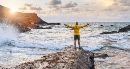 Person in yellow jacket standing on rock by the sea with arms wide open at sunset- Stock Photo or Stock Video of rcfotostock | RC Photo Stock