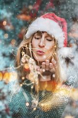 Portrait of a young woman wearing a Christmas hat in a winter landscape blowing snow out of her hand- Stock Photo or Stock Video of rcfotostock | RC Photo Stock