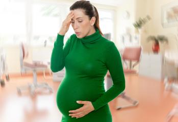 Pregnant woman in a green dress holding her belly and forehead, exhaling deeply, appearing to manage labor pain or discomfort in a brightly lit medical or clinic environment : Stock Photo or Stock Video Download rcfotostock photos, images and assets rcfotostock | RC Photo Stock.: