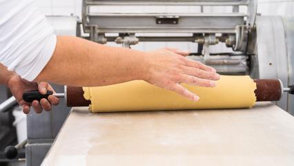 Rolling out cookie dough with a wooden rolling pin in a bakery, preparing the dough for cutting, with a hand steadying the dough in a professional baking environment- Stock Photo or Stock Video of rcfotostock | RC Photo Stock