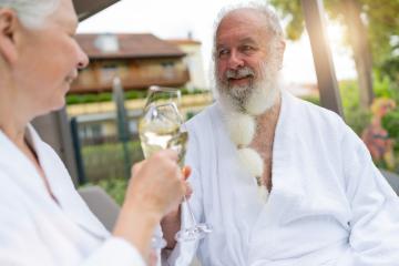 Senior couple in white bathrobes clinking champagne glasses, man looking at woman at spa hotel resort- Stock Photo or Stock Video of rcfotostock | RC Photo Stock