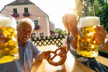 Senior man and young woman in Bavarian tracht holding beer mugs and pretzel, smiling at camera in a beer garden or Oktoberfest, Munich, Germany- Stock Photo or Stock Video of rcfotostock | RC Photo Stock