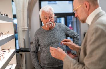 Senior man listening to optician holding a new eyewear model in hands in optical store : Stock Photo or Stock Video Download rcfotostock photos, images and assets rcfotostock | RC Photo Stock.: