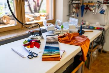 sewing or tailoring workshop showcases a table filled with sewing essentials: fabric swatches, scissors, iron, color palette, silk fabrics and tools, with a window displaying stacked firewood outside- Stock Photo or Stock Video of rcfotostock | RC Photo Stock
