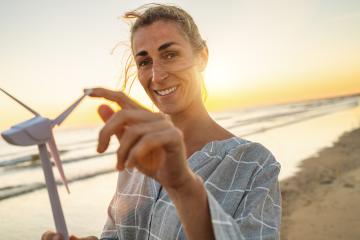 Smiling  woman holding wind turbine model at sunset on the beach. Wind Turbines Windmill Energy Farm concept image : Stock Photo or Stock Video Download rcfotostock photos, images and assets rcfotostock | RC Photo Stock.: