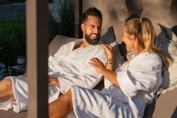 Smiling and talking couple in white bathrobes enjoying a conversation in the sunlight at spa hotel- Stock Photo or Stock Video of rcfotostock | RC Photo Stock