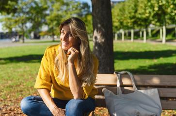 smiling blonde woman sitting outdoor and thinking. woman relaxing on a wooden bench with canvas fabric bag under the tree in a summer day. Portrait of woman smiling and daydreaming- Stock Photo or Stock Video of rcfotostock | RC-Photo-Stock