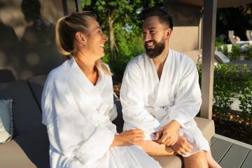 smiling couple in white bathrobes enjoying a sunny day outdoors on a couple's lounger at a spa hotel- Stock Photo or Stock Video of rcfotostock | RC Photo Stock