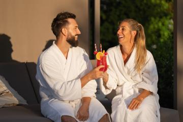 Smiling couple in white spa robes clinking cocktails in sunny ambiance at spa resort- Stock Photo or Stock Video of rcfotostock | RC Photo Stock