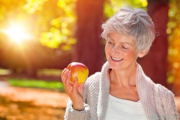Smiling elderly woman holding an apple outdoors in autumn sunlight with a serene background : Stock Photo or Stock Video Download rcfotostock photos, images and assets rcfotostock | RC Photo Stock.: