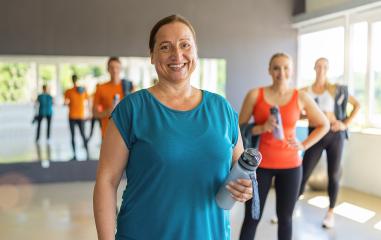 Smiling older woman holding a water bottle in a gym with other participants in the background. Teamwork Concept image : Stock Photo or Stock Video Download rcfotostock photos, images and assets rcfotostock | RC Photo Stock.: