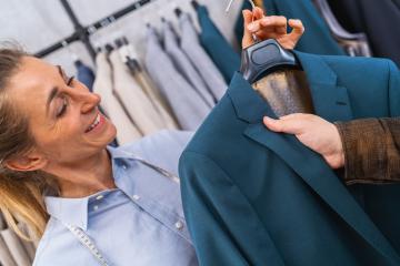 Smiling sailswoman showing a teal jacket to a male customer, clothes racks in the background at weeding store : Stock Photo or Stock Video Download rcfotostock photos, images and assets rcfotostock | RC Photo Stock.: