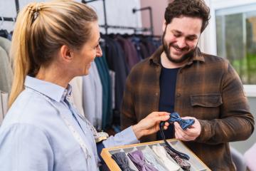 Smiling tailor showing a blue bow tie to a happy male customer, suits in the background : Stock Photo or Stock Video Download rcfotostock photos, images and assets rcfotostock | RC Photo Stock.: