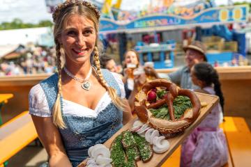 Smiling Waitress in traditional Bavarian dress or dirndl holding a wooden platter with traditional German food in a beer tent at  oktoberfest festival or dult in germany- Stock Photo or Stock Video of rcfotostock | RC Photo Stock