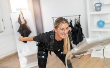 Smiling woman doing an upper body twist in EMS training gear with a trainer nearby at a EMS-Studio- Stock Photo or Stock Video of rcfotostock | RC Photo Stock