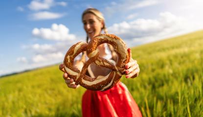 Smiling woman in Bavarian dirndl holding a large pretzel in front of a wheat field celebrating Oktoberfest or dult festival in munich.- Stock Photo or Stock Video of rcfotostock | RC Photo Stock