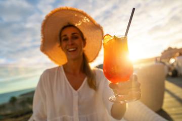 Smiling woman in straw hat holding a cocktail against a sunset backdrop- Stock Photo or Stock Video of rcfotostock | RC Photo Stock