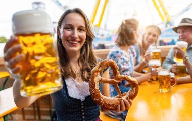 Smiling woman in traditional dress or dirndl holding a beer mug and a pretzel, with friends drinking in the background at oktoberfest in munich or dult in germany- Stock Photo or Stock Video of rcfotostock | RC Photo Stock