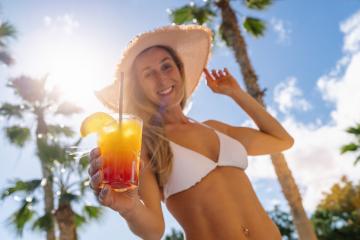 Smiling woman in white bikini and straw hat holding a tropical cocktail, palm trees, sunny sky at caribbean island- Stock Photo or Stock Video of rcfotostock | RC Photo Stock