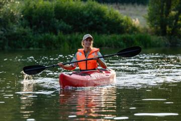 smiling woman kayaking on a calm river, paddling with a black oar, wearing an orange life jacket and cap in germany at summer. Kayak Water Sports concept image : Stock Photo or Stock Video Download rcfotostock photos, images and assets rcfotostock | RC Photo Stock.: