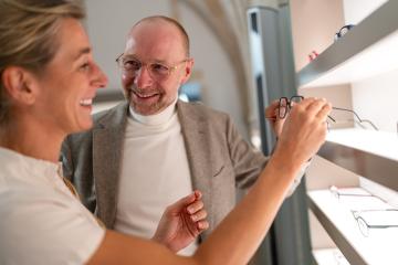 smiling woman selecting eyeglasses with optician in a store. shelf with glasses in the background- Stock Photo or Stock Video of rcfotostock | RC Photo Stock