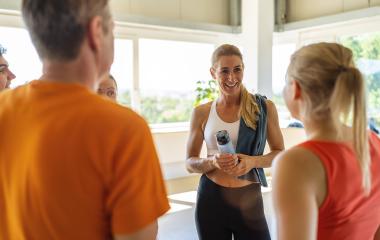 Smiling woman with a water bottle talking to other gym members in a sunny room- Stock Photo or Stock Video of rcfotostock | RC Photo Stock