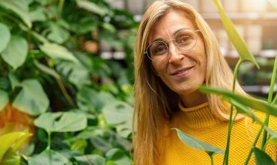 Smiling woman with glasses amidst green flowers looking in to camera in a Garden Center for Purchase. Shopping in a greenhouse concept image : Stock Photo or Stock Video Download rcfotostock photos, images and assets rcfotostock | RC Photo Stock.: