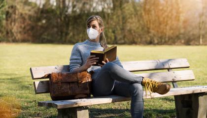 Student girl sitting on bench in park and read a book with protection mask to prevent others from corona COVID-19 and SARS cov 2 infection. social distancing concept image- Stock Photo or Stock Video of rcfotostock | RC Photo Stock