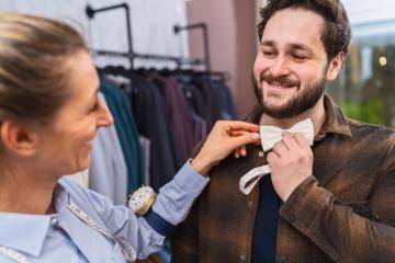 Tailor adjusting a bow tie for a smiling male customer, clothes racks in a wedding shop- Stock Photo or Stock Video of rcfotostock | RC Photo Stock