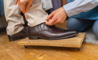 Tailor adjusts a man's trouser length over a brown shoe on a wooden footrest : Stock Photo or Stock Video Download rcfotostock photos, images and assets rcfotostock | RC Photo Stock.: