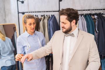 Tailor examining sleeve length on a man's suit in a clothing shop with a concerned expression- Stock Photo or Stock Video of rcfotostock | RC Photo Stock