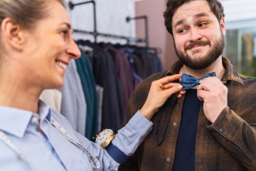 Tailor fitting a blue bow tie on a customer, both smiling, with clothing in background : Stock Photo or Stock Video Download rcfotostock photos, images and assets rcfotostock | RC Photo Stock.: