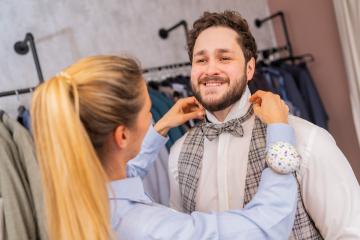 Tailor fitting a bow tie on a cheerful man in a fashion store with clothing racks
 : Stock Photo or Stock Video Download rcfotostock photos, images and assets rcfotostock | RC Photo Stock.: