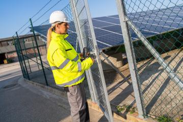 Technician in high visibility jacket on a gate with walkie-talkie at solar farm. Alternative energy ecological concept image.- Stock Photo or Stock Video of rcfotostock | RC Photo Stock