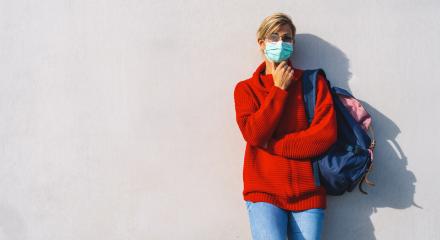 thoughtful woman in glasses and a teal face mask leans against a concrete wall. She wears a red sweater,jeans, and carries a backpack, with one hand resting beneath her chin, with copyspace : Stock Photo or Stock Video Download rcfotostock photos, images and assets rcfotostock | RC Photo Stock.:
