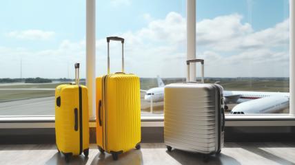 Three suitcases, two yellow and one silver, stand by a large airport window. In the background, airplanes are visible on the tarmac under a partly cloudy sky- Stock Photo or Stock Video of rcfotostock | RC Photo Stock