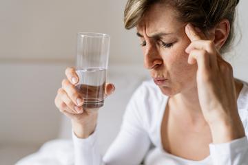 tired woman touching forehead and holding glass with water having headache migraine or depression, feel stressed grabs head with hand with pain sit on bed in the morning, Flu or overload Concept - Stock Photo or Stock Video of rcfotostock | RC-Photo-Stock