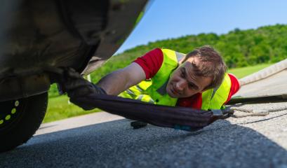 Tow truck worker inspecting a car underneath after an accident to prepare it with tow rope for transport on the roadside : Stock Photo or Stock Video Download rcfotostock photos, images and assets rcfotostock | RC Photo Stock.: